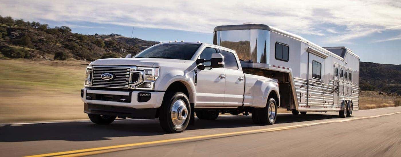 A white 2020 Ford F-450 Super Duty is shown towing a trailer on an open road.