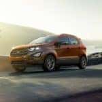 An orange 2020 Ford EcoSport is shown from the side driving on an open road after leaving a used Ford SUV dealer.