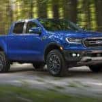A popular used truck for sale, a blue 2019 Ford Ranger is shown driving on a dirt road.