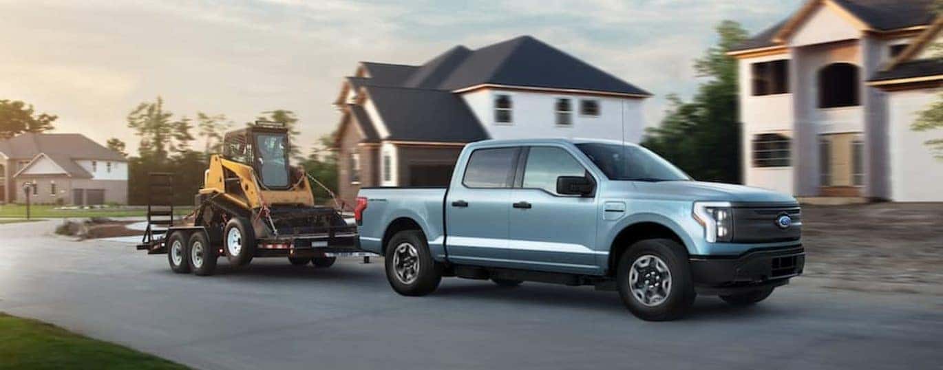 A blue 2022 Ford Lightning is shown towing machinery through a neighborhood.