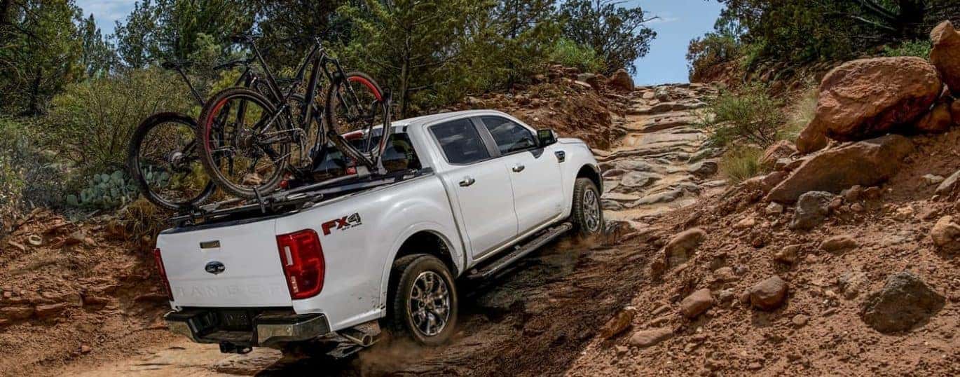 A white 2022 Ford Ranger Lariat is shown off-roading on a steep rocky trail.