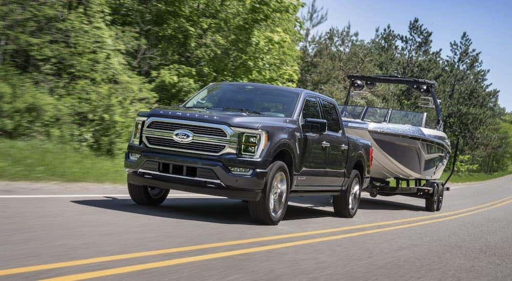 A grey 2022 Ford F-150 Platinum is shown from the front at an angle while it tows a boat down a road.
