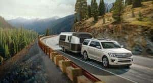 A white 2020 Ford Expedition is shown towing a camping trailer on an open highway.