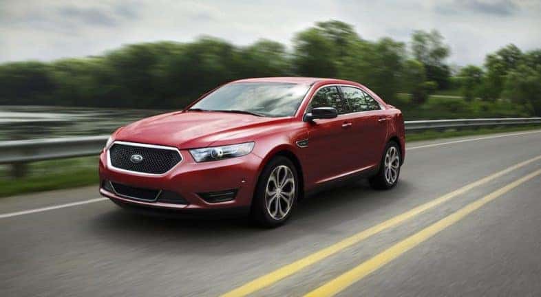 A 2017 Ford Taurus SHO is shown from the front at an angle while driving down the highway after the owner searched 'used car dealerships Albany, NY'.