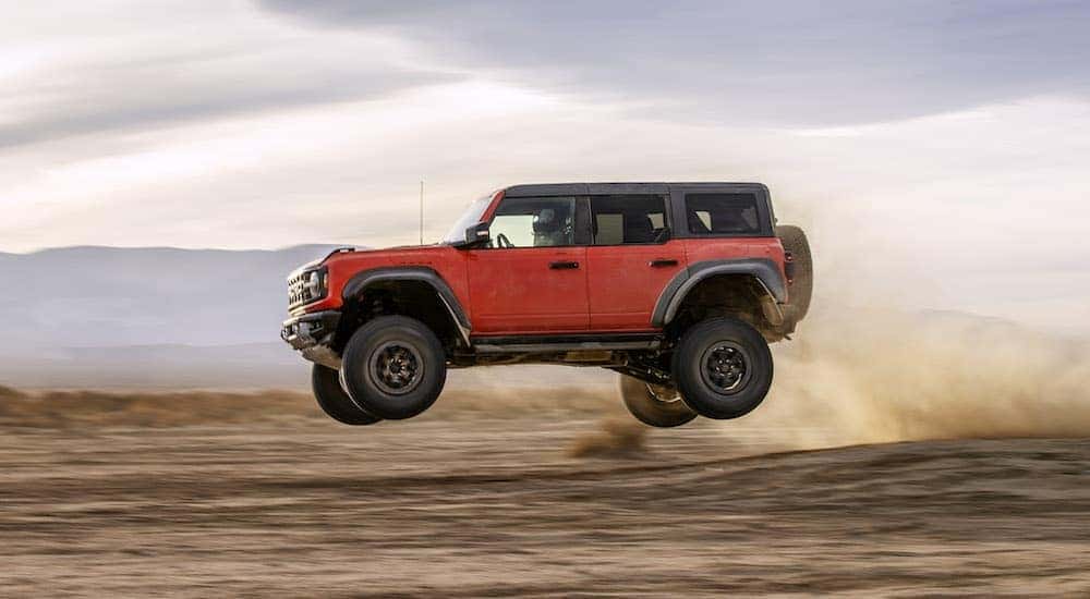 Red 2022 Ford Bronco Raptor is shown from the side while jumping through the air after leaving a car dealership in Albany, NY.