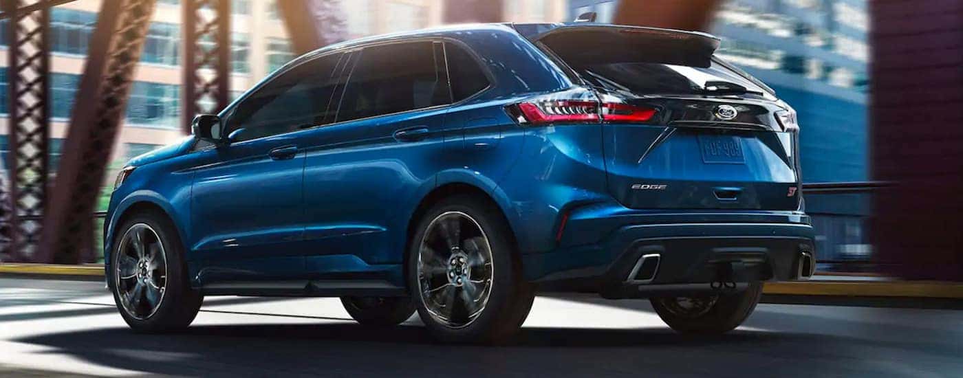 A blue 2019 Ford Edge ST is shown from the rear driving over a bridge after searching "used car dealers near me."