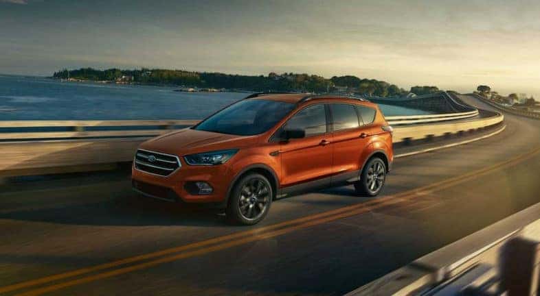 An orange 2019 Ford Escape is shown from the side driving past a body of water.