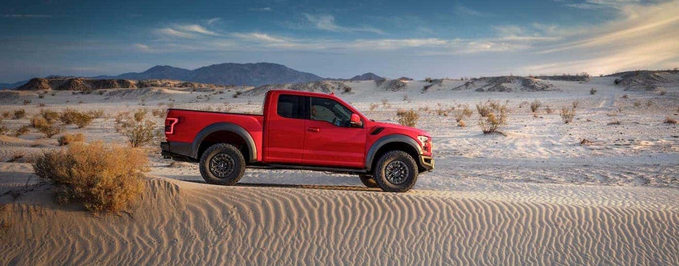 A red 2019 Ford Raptor is shown from the side driving through a desert.