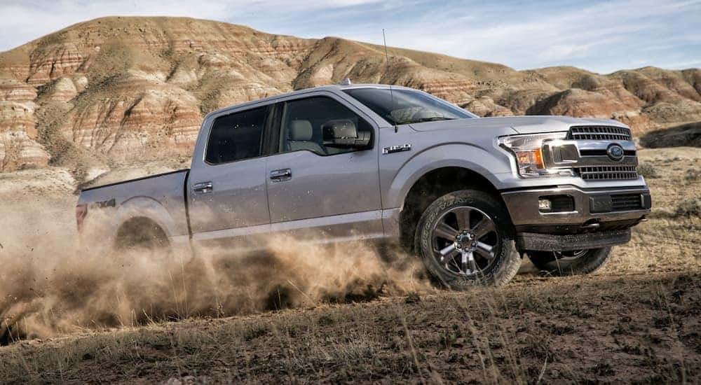 A popular used Ford F-150, a silver 2020 Ford F-150, is shown from the side off-roading in a field.