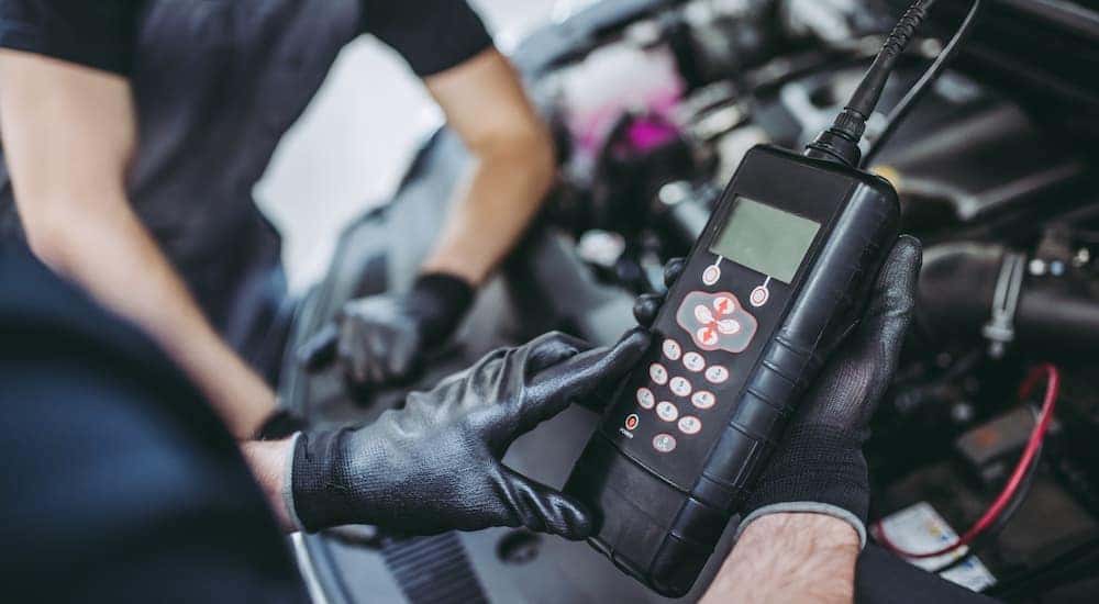 A mechanic is shown using an OBD reader under the hood of a car.