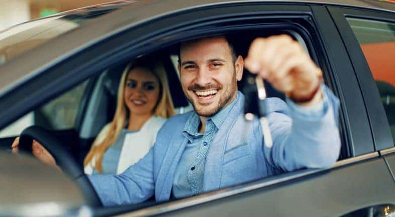 A couple is shown sitting in the front seat of a car at a Ravena used Ford dealer.