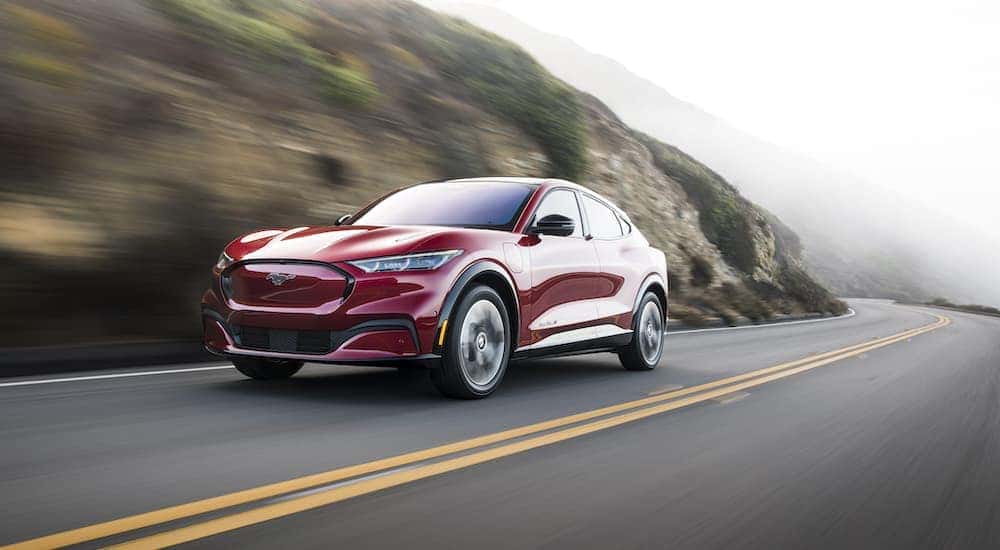 A red 2022 Ford Mustang Mach-E is shown driving past a rock face.