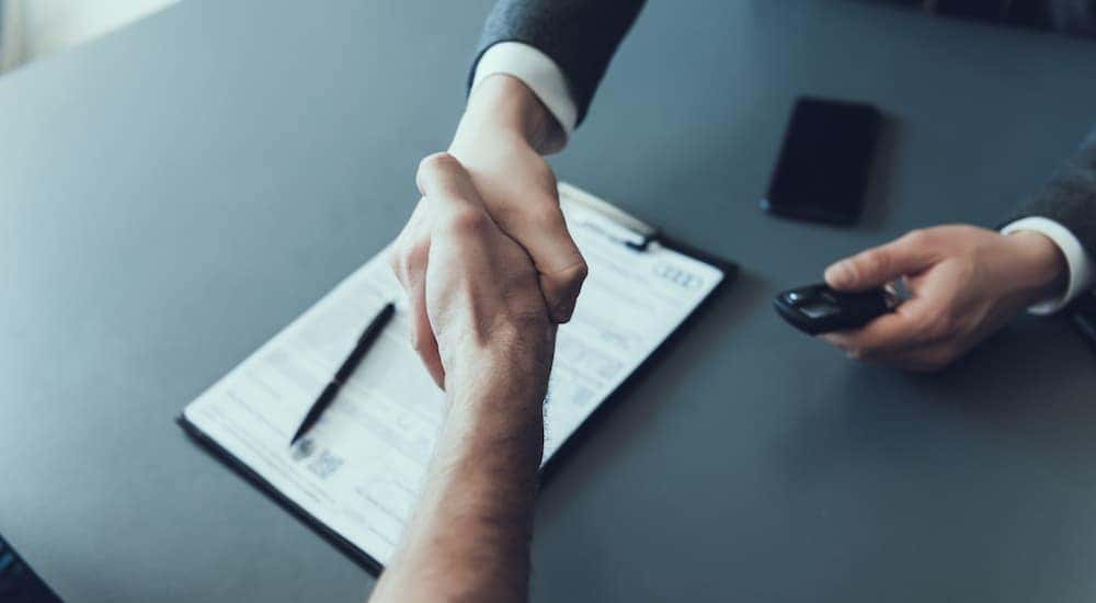 A salesman is shown shaking hands with a customer over paperwork.