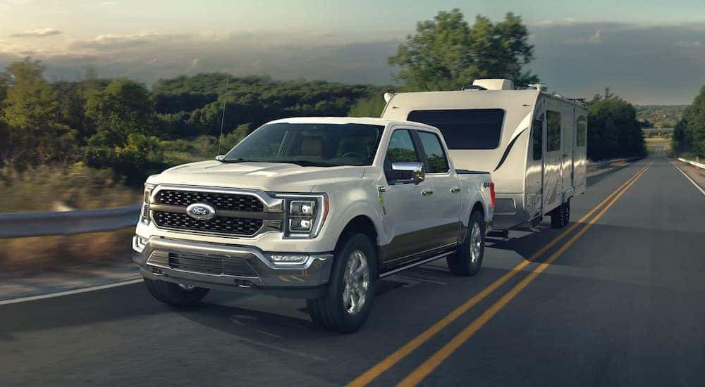 A white 2021 Ford F-150 is shown towing a trailer near mountains.