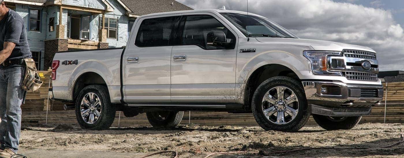 A popular used Ford for sale, a silver 2020 Ford F-150, is shown from the side parked at a construction site.