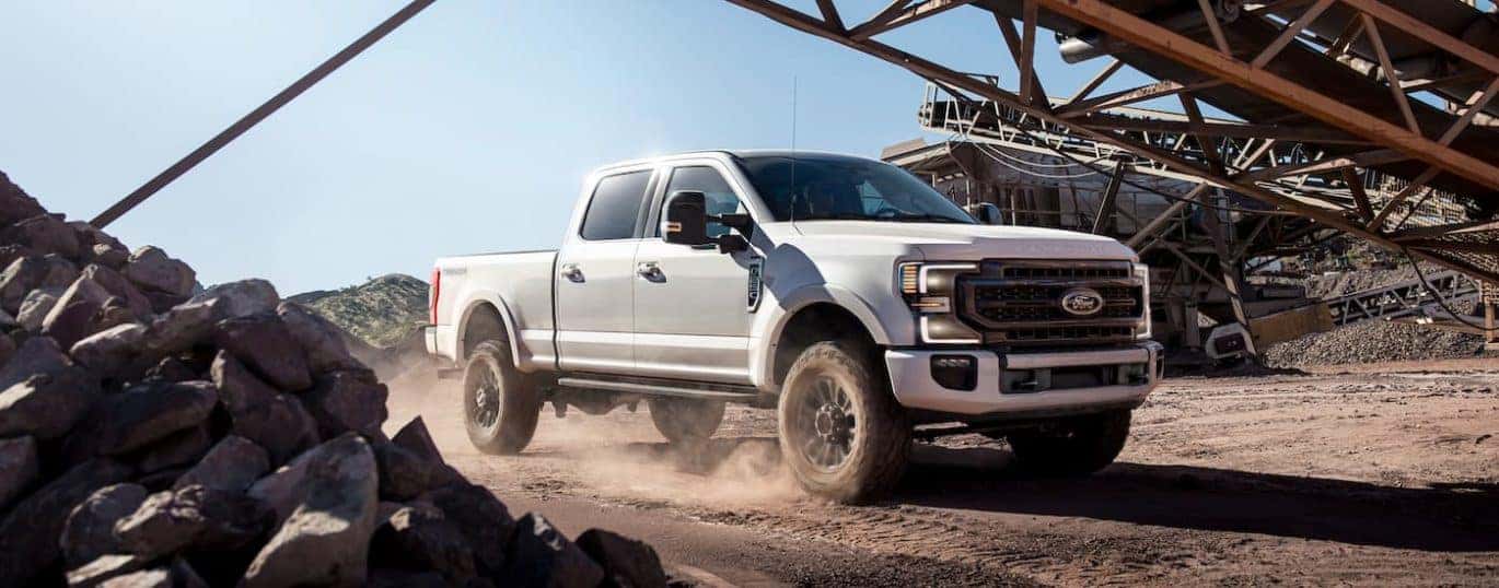 A white 2023 Ford F-250 Tremor is shown from the front at an angle while driving through a jobsite.