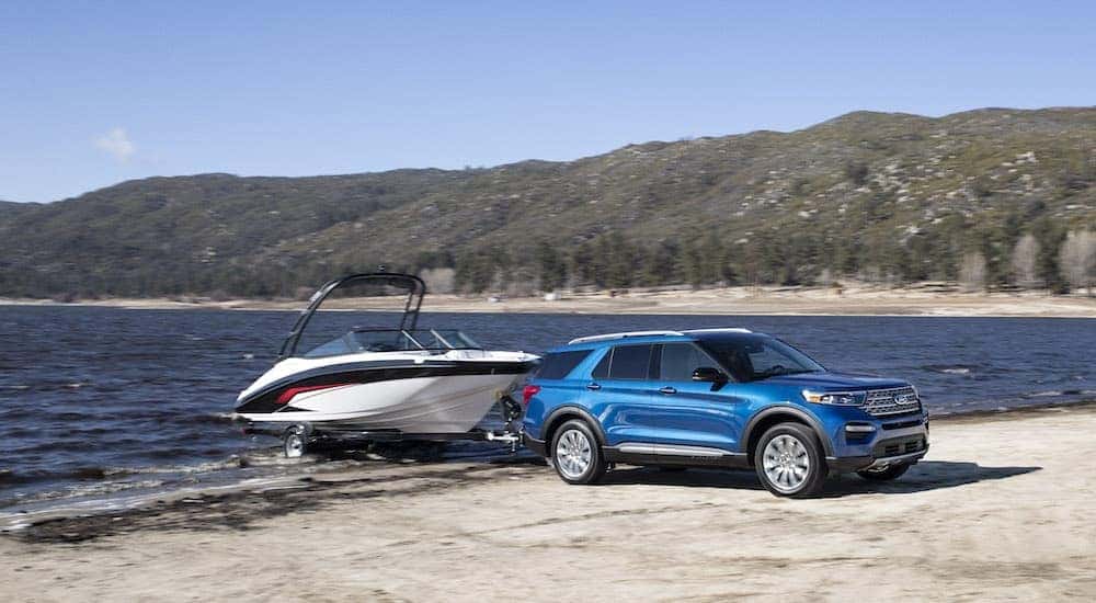 A blue 2020 Ford Explorer Hybrid is shown towing a boat near a lake.