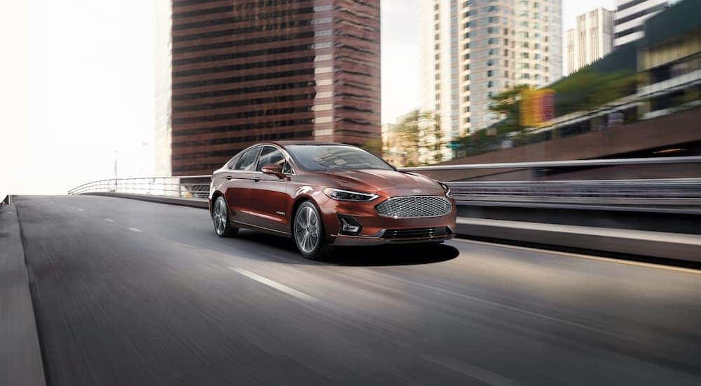 A red 2020 Ford Fusion Titanium Hybrid is shown driving on a city street after leaving an Albany used Ford dealer.