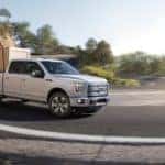 A white 2015 Ford F-150 is shown rounding a corner with a crate in the bed.