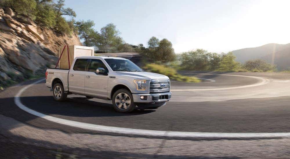 A white 2015 Ford F-150 is shown rounding a corner with a crate in the bed.