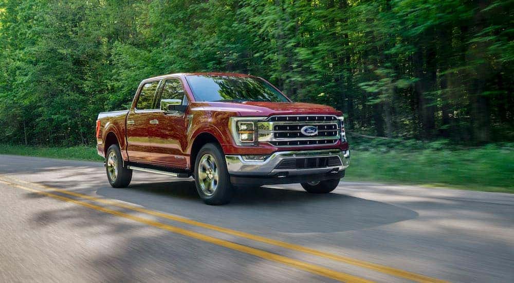 A popular used Ford F-150 for sale, a red 2020 Ford F-150 Lariat, is shown driving on a tree-lined road.