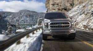 A silver 2022 Ford F-150 Platinum is shown driving on a snowy mountain highway.