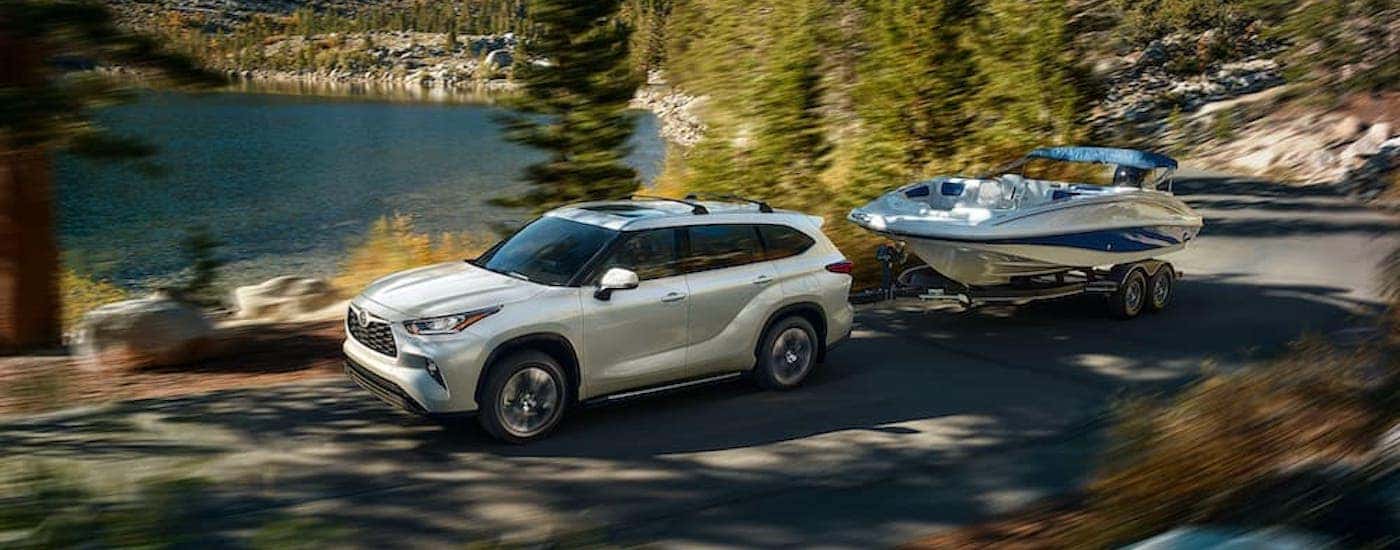A white 2020 Toyota Highlander is shown from the side while towing a boat after leaving an Albany, NY used SUV dealer.