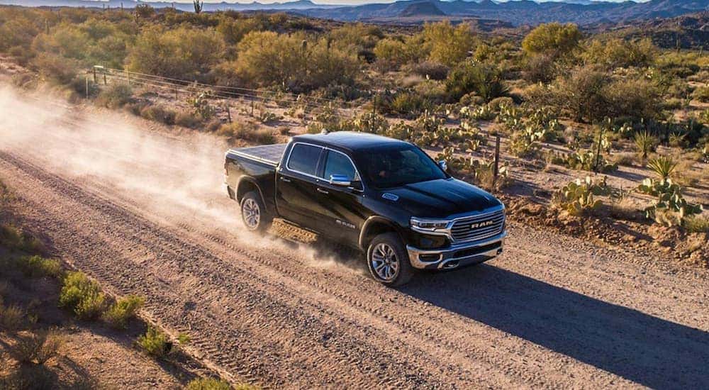 A black 2020 Ram 1500 is shown driving on a dirt road.