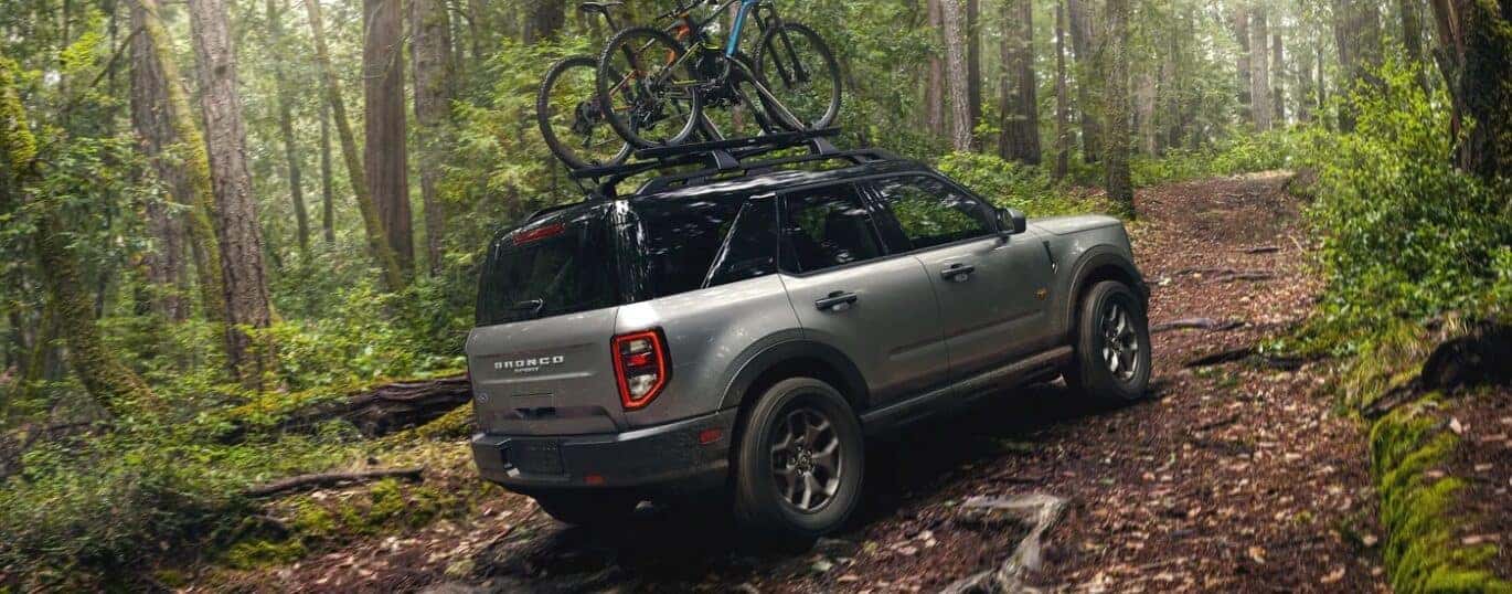 A silver 2023 Ford Bronco Sport Badlands is shown from a rear angle driving on a forest trail.