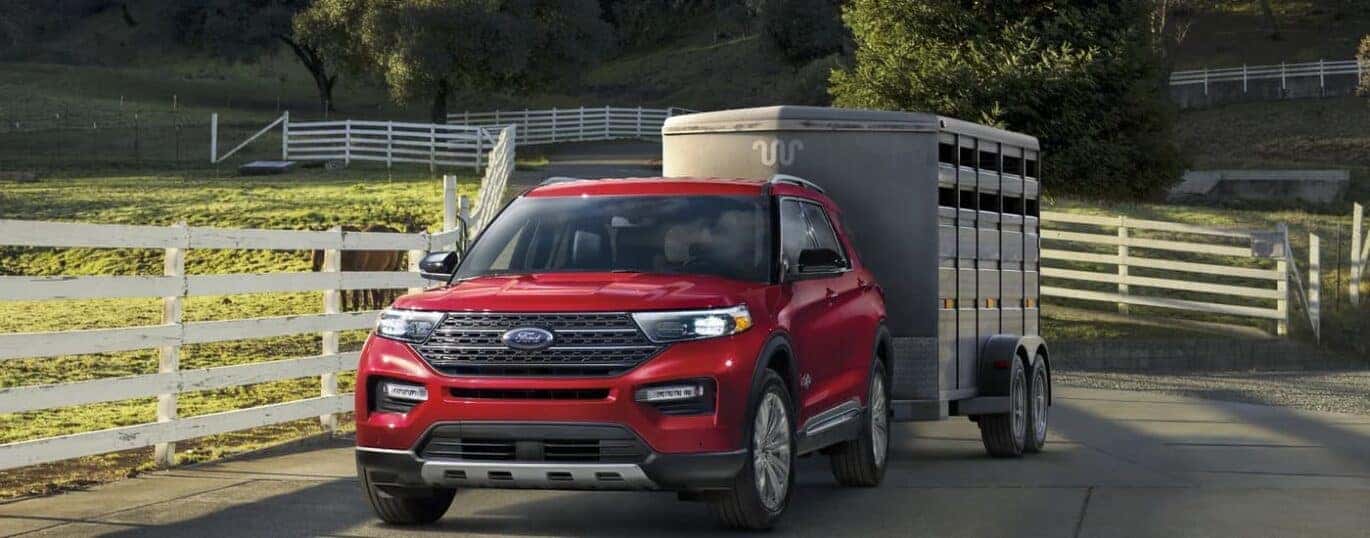 A red 2023 Ford Explorer is shown towing a horse trailer on a farm.