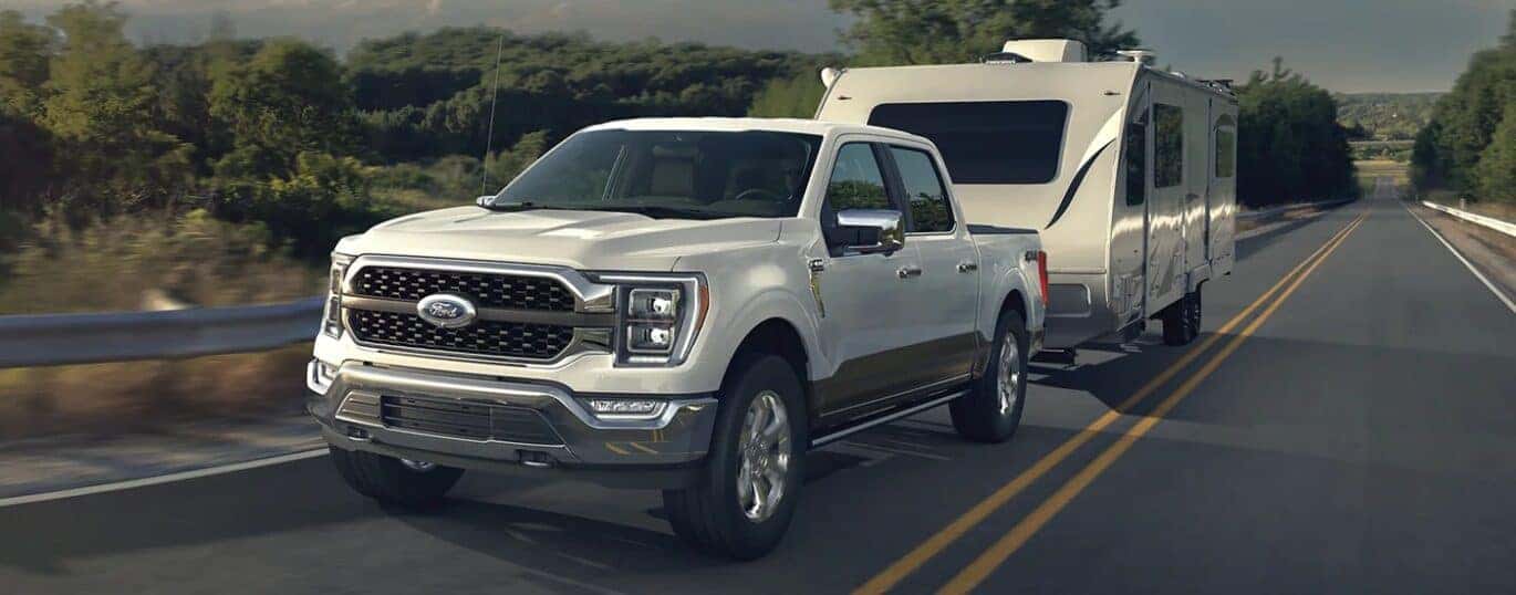 A white 2023 Ford F-150 is shown towing a trailer on a highway.