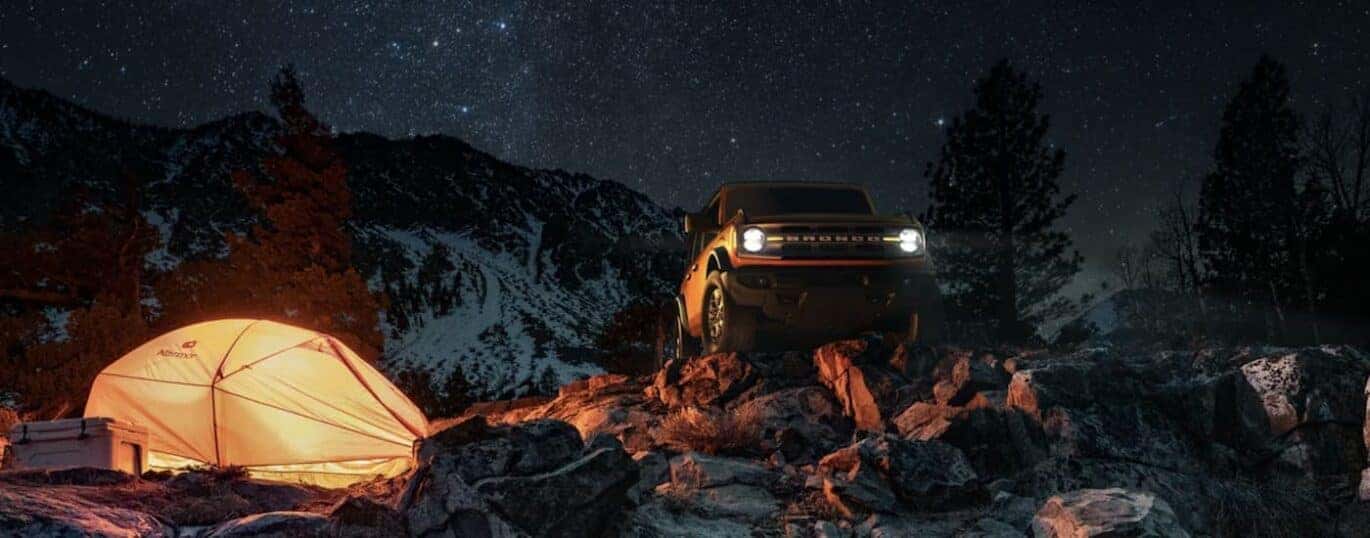 An orange 2023 Ford Bronco is shown parked in the mountains at night.