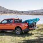 An orange 2022 Ford Maverick Lariat is shown from the side while parked on a lakeshore.
