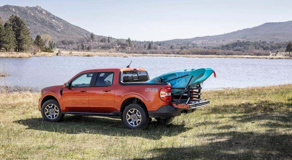 An orange 2022 Ford Maverick Lariat is shown from the side while parked on a lakeshore.