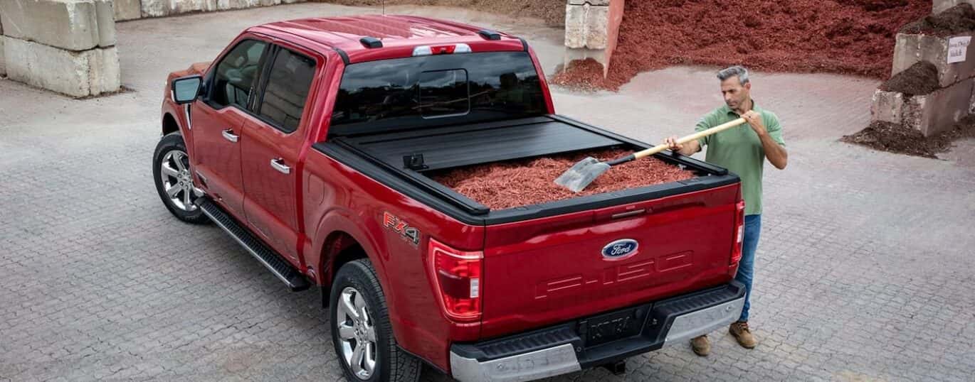 A red 2023 Ford F-150 is shown from the rear with a bed full of mulch.
