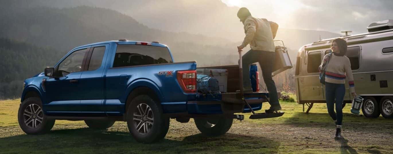 A blue 2023 Ford F-150 STX is shown from the side at a campsite.