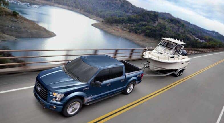 A blue 2017 Ford F-150 XLT is shown towing a fishing boat near a body of water.