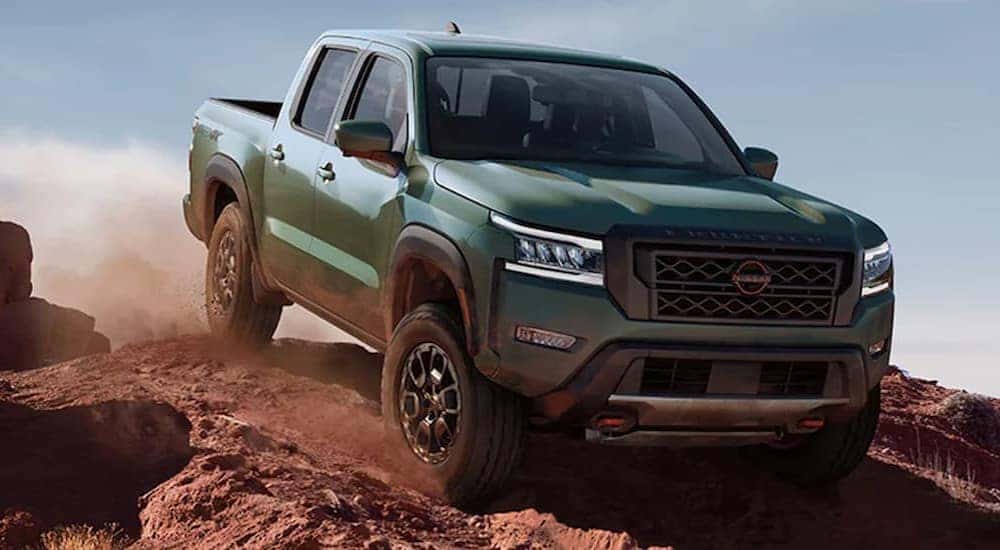 A green 2022 Nissan Frontier is shown off-roading on a dirt path.