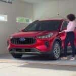 A person is shown charging a red 2023 Ford Escape Hybrid in a garage.