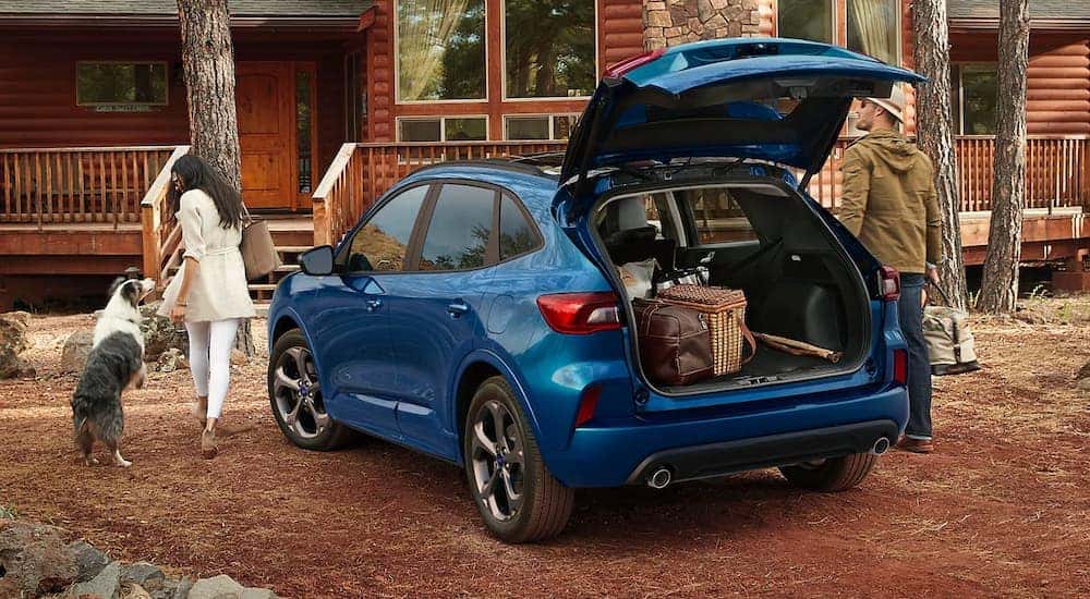 A blue 2023 Ford Escape for sale it shown parked near a cabin.