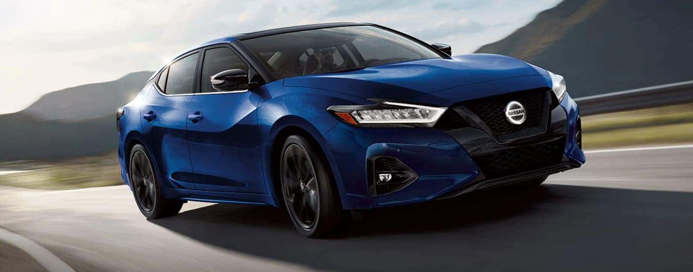 A blue 2021 Nissan Maxima is shown driving on an open highway.