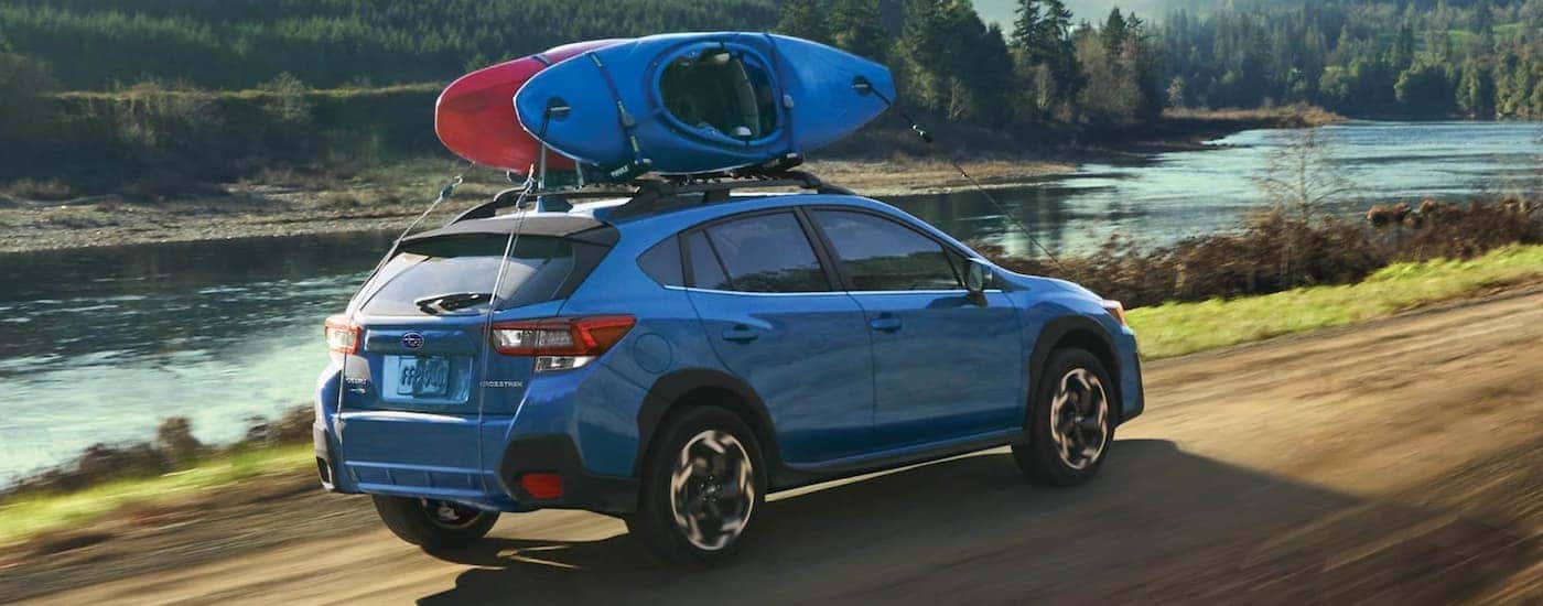 A blue 2021 Subaru Crosstrek is shown with kayaks driving next to a river.