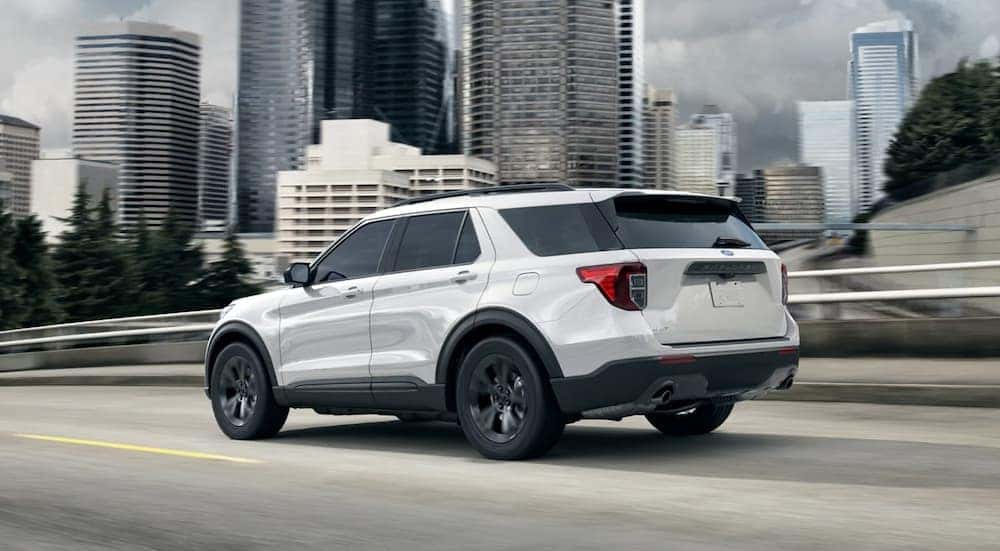 A white 2021 Ford Explorer is shown driving past city buildings.