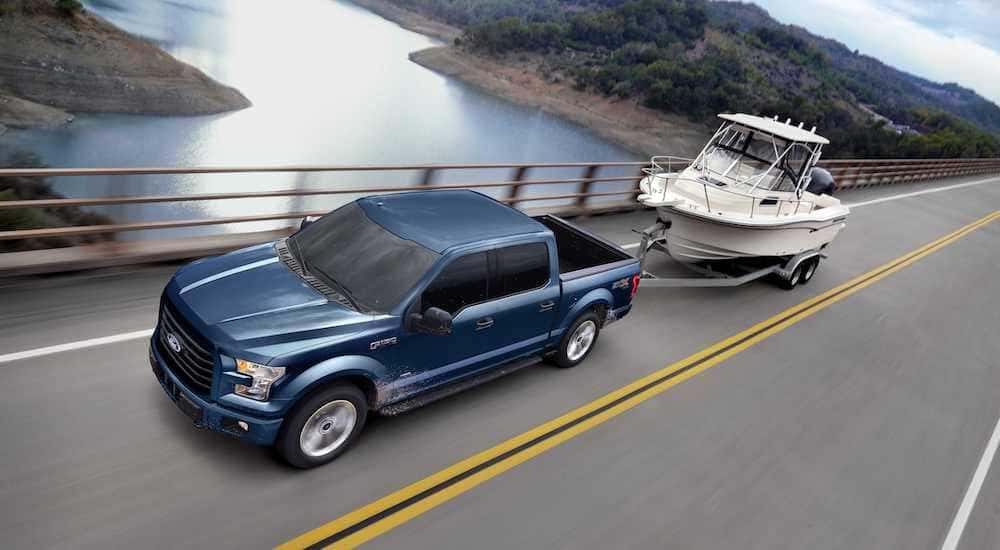 A blue 2017 Ford F-150 is shown towing a boat after looking at used cars for sale.