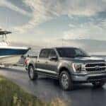 A silver 2022 Ford F-150 Limited is shown towing a boat past a lake.