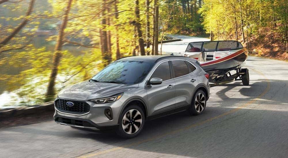A silver 2024 Ford Escape is shown towing a boat near water.