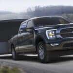 A popular used truck for sale, a black 2021 Ford F-150 Limited, is shown towing a boat on a highway.
