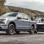 One of many popular used trucks for sale in Albany, NY, a gray 2023 Ford F-150 Lightning, is shown towing a boat.