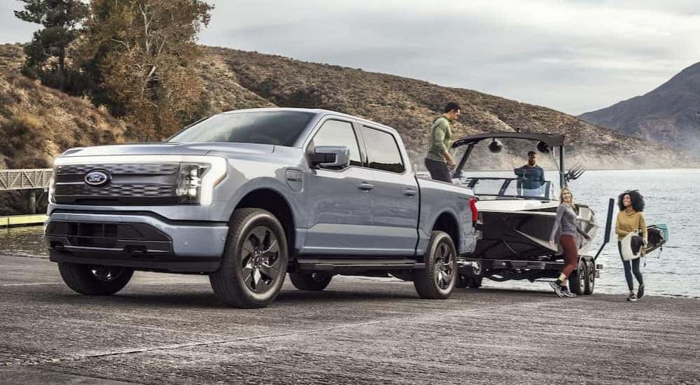 One of many popular used trucks for sale in Albany, NY, a gray 2023 Ford F-150 Lightning, is shown towing a boat.