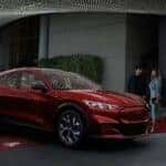 A red 2022 Ford Mustang Mach-E is shown parked on a red carpet under lights.